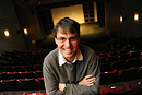 A man smiles in a portrait with a theatre stage as a backdrop