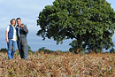 Two farmers pose in their field with a huge oak tree in the background