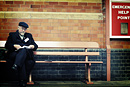 A man seated on a bench gets his papers in order while waiting for a train